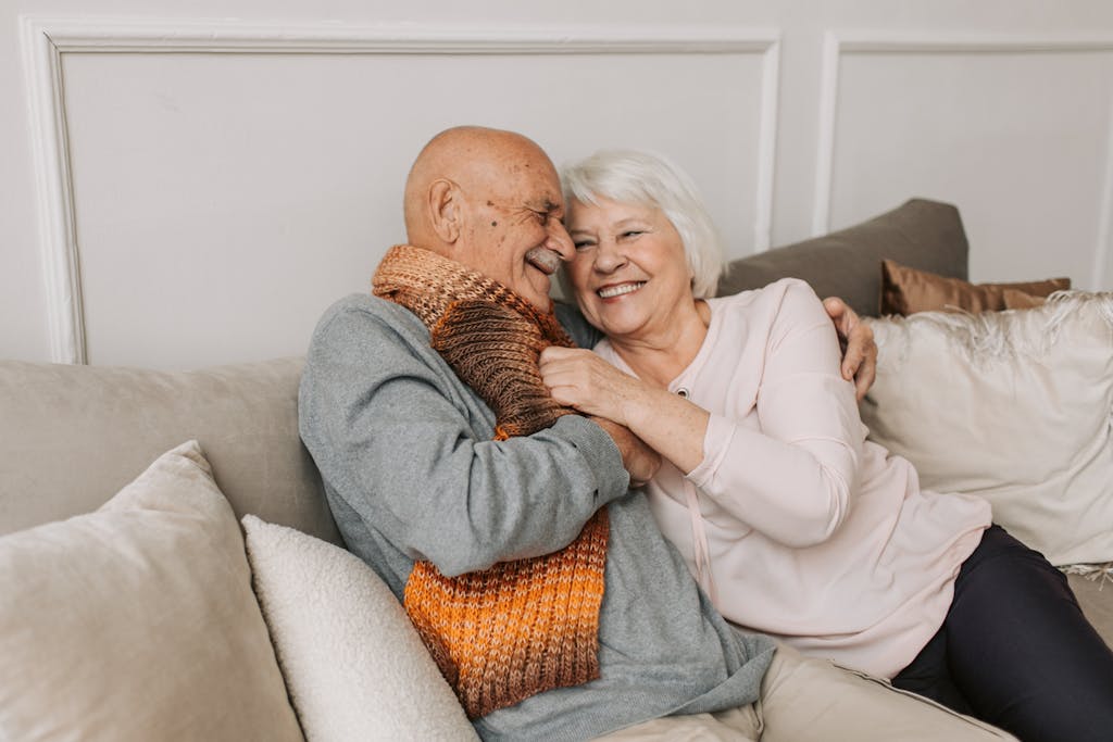 Happy elderly couple embraced in a cozy home setting, sharing joyful smiles.